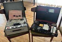 Sony TC-200HR tape recorder open showing controls, two tape spools and instruction manual inside lid. Beside it is an open black case with red interior containing various accessories spread neatly.
