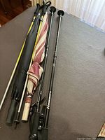 Photo showing two black exercise walking sticks with grips and two large umbrellas, one black and one striped maroon and beige.