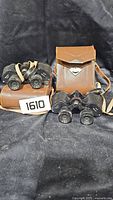 Two black Spächer Wetzlar binoculars placed on and beside brown leather carrying cases on a black fabric background.
