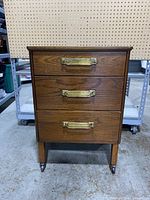 Front view of the three-drawer oak medical cabinet showing brass handles and wood grain finish.
