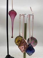 Photo showing grouping of five blown glass ornaments hanging from stands, various colors and shapes including long teardrop, round, and diamond-shaped ornaments.