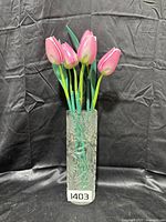 Tall clear rectangular crystal vase with floral-textured sides holding six wooden pink tulip flowers with green stems and leaves.