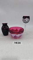 Lot of three decorative glass pieces, includes a small purple etched vase, a decorative bowl with clear and purple glass, and a tall etched wine glass. All items shown from front view.