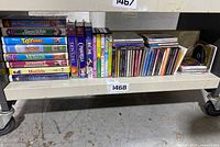 Shelf holding a selection of Disney VHS tapes to the left and a collection of music CDs to the right. VHS includes titles such as Toy Story, Lion King, Cinderella, The Little Mermaid, Matilda.
