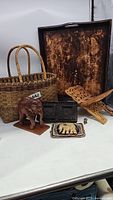 Photo showing the entire grouping of ethnic decor items including basket, elephant statue, tray, book stand, carved pieces, and wood stamp.