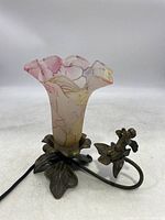 Side angle showing frosted pink and yellow tulip glass shade on metal base with leaf pattern and cherub figure on curved arm.
