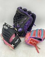 Three used child's Rawlings baseball/softball gloves, black/pink, black/purple, and pink/blue color schemes.
