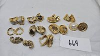 Photo of 10 pairs of vintage clip-on earrings arranged on white cloth with auction lot number 664 visible.