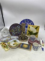 Grouping of various handpainted ceramic items with floral and scenic designs including plates, tiles, cups, decorative dishes, candlestick holder.
