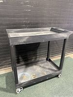 Front view of the black fiberglass industrial rolling cart showing two shelves and caster wheels.