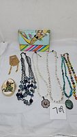 Full lot with purse, porcelain pill box, bracelets, and necklaces laid out on white.