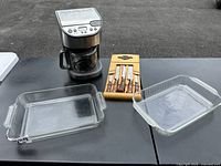 Lot overview showing all items on table: coffee maker, two glass baking dishes, and wooden block with knives.