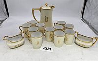 Full set including pitcher, eleven cups, sugar bowl, and creamer arranged and showing the monograms and gold trim.