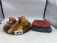 Photo showing wooden Lazy Susan with three sugar bowls and one creamer on top and stacks of red and teal plates to the side