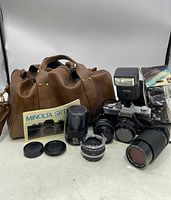 Full view of Minolta SRT SC-II camera, lenses, flash, manuals, and leather carry bag all arranged together