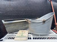Fiberglass planter, farmhouse bucket, and floral handmade wall hanging on white wire rack against black backdrop.