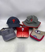 Five pieces of Philadelphia Phillies headwear arranged on a white surface showing front logos.