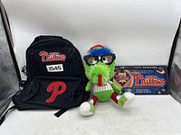 Front view displaying the black Phillies backpack, Phillie Phanatic plush toy with glasses, and Phillies license plate with holder.