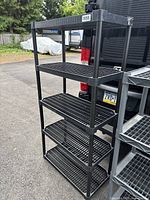 Full view of black plastic shelving unit standing approximately 6 feet tall outdoors on asphalt surface next to vehicle