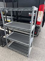 Full view of gray plastic shelving unit next to vehicle showing 4-tier shelves and tubular legs.