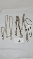 Photo showing eight pieces of silver-tone jewelry on white background including various necklaces and bracelets, some with heart and star pendants.
