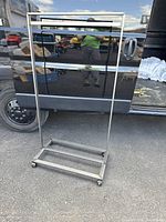 Front view of small metal clothing rack showing rectangular base on caster wheels and single horizontal hanging bar.
