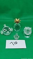 Full lot showing four Swarovski crystal figurines on green background, including fish, pineapple, owl, and small bird.