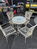 Photo showing entire patio set with one round table and four chairs arranged around it outdoors on pavement.