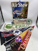 Photo shows 3 sports pennants (Philadelphia Eagles, Philadelphia Phillies, Tampa Bay Rays), 1975 Willow Grove Air Show poster with Eagles sticker, and vintage Eagles and Tug McGraw buttons.