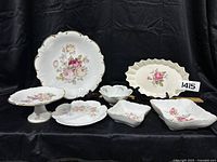 Full set of vintage rose serving dishes including large platters, pedestal cake stand, scalloped plates and bowls with gold trim and floral designs.