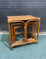 Set of three wicker bamboo nesting tables stacked together showing natural wear and damage