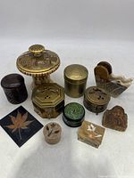 Photo showing the full lot of 11 small trinket boxes in various materials and shapes including brass, marble, wood, and enamel decorative finishes.