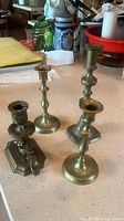 Five assorted bronze candle holders of various sizes arranged on a counter, showing bases and stems