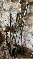 Photo of bronze vintage fireplace tools set leaned against a stone wall, showcasing detailed handles and bronze finish.