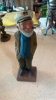 Front view of carved wooden captain figure with white cap, blue shirt, khaki jacket, and pipe