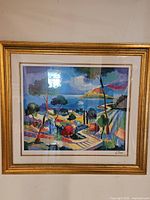 Framed colorful seriolitograph painting depicting French Riviera landscape with water, trees, and sky, signed by artist in bottom right corner.