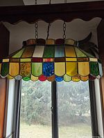 Front view of hanging Tiffany style stained glass pool table lamp showing multi-colored panels in green, yellow, red, blue, with scalloped edging, hung by metal chains.