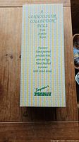 Original box with yellow and white striped design and green text describing the doll as a Connoisseur Collection doll by Seymour Mann, hand painted porcelain head, arms, and legs, hand finished costumes with lavish detail.