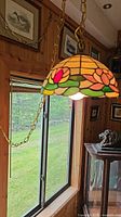 Pendant lamp with stained glass floral shade hanging by metal chain next to window in wooden room