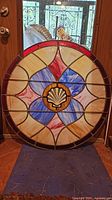 Front view of large stained glass panel with central shell motif and red, blue, cream colored glass segments