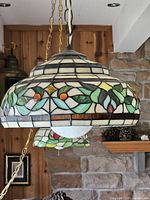Close-up side view of Tiffany style pendant lamp showing stained glass panels with floral and leaf design in green, orange, yellow.