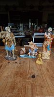 Four vintage Asian porcelain figurines arranged on wooden surface showing variety of poses and colors