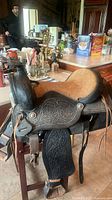 Side view of the vintage leather saddle showing floral tooling, suede seat, and leather straps.