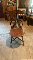 Front view of vintage wooden chair showing carved top rail, spindle back, and rounded wooden seat.