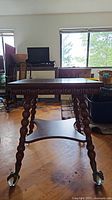 Full view of the antique wooden table showing the distinct carved legs with spherical patterns and clawed feet with casters under a square top.