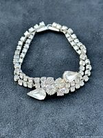 Close-up photo of vintage rhinestone necklace showing front details including large teardrop-shaped rhinestones and smaller round rhinestones in a cluster, with two rows of smaller rhinestones forming the chain.