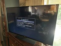 Front view of the TV powered on showing “No Cable Connected” message, mounted on stand over wooden cabinet