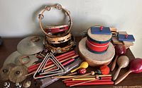 Collection of assorted vintage children's musical percussion instruments including tambourines, drums, maracas, cymbals, castanets, triangle, and rhythm sticks.