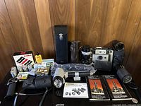Wide view of entire lot showing cameras, lenses, flash, flashbulbs, manuals, and cases on wooden panel background.