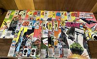 Photo showing an array of 22 vintage GI-JOE comic books arranged on a wood surface with colorful covers and various character artwork.